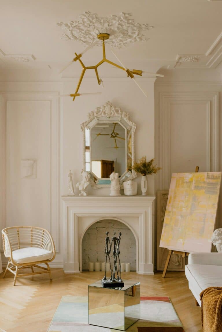 Image of a white fireplace in a living room with a white chair and a painting on an easel.